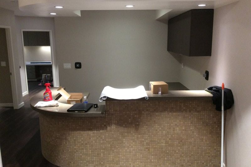A modern reception desk with a tiled front, cleaning supplies, boxes, and dim recessed lighting above.